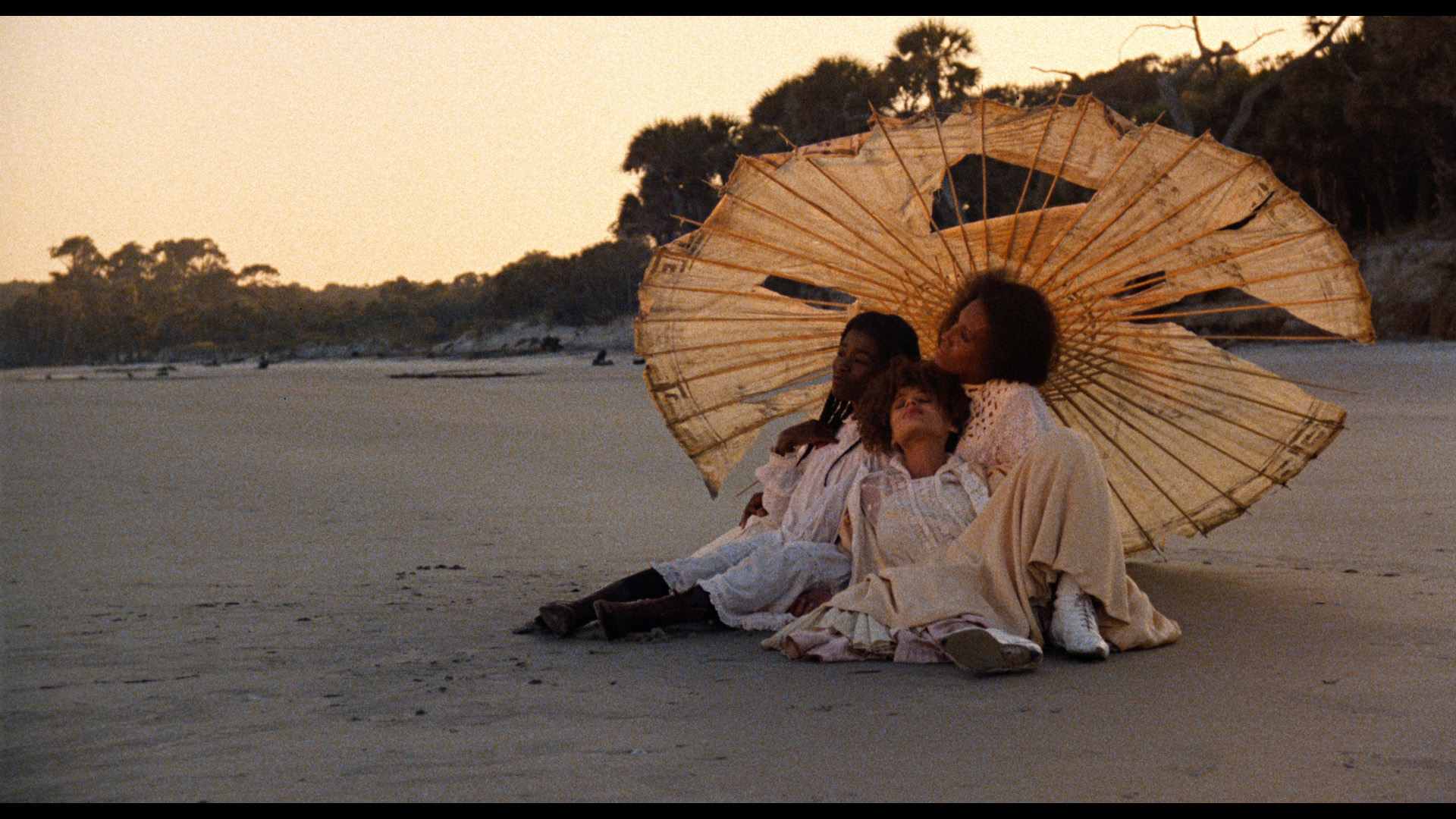 3 women laying under the shade on a beach.